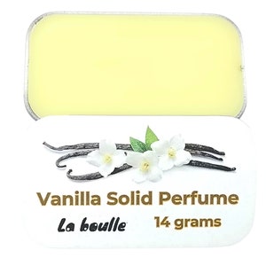 May include: A white tin with a yellow solid perfume inside. The tin has a label that says "Vanilla Solid Perfume" and "La Bouille" with a vanilla bean and white flower design.