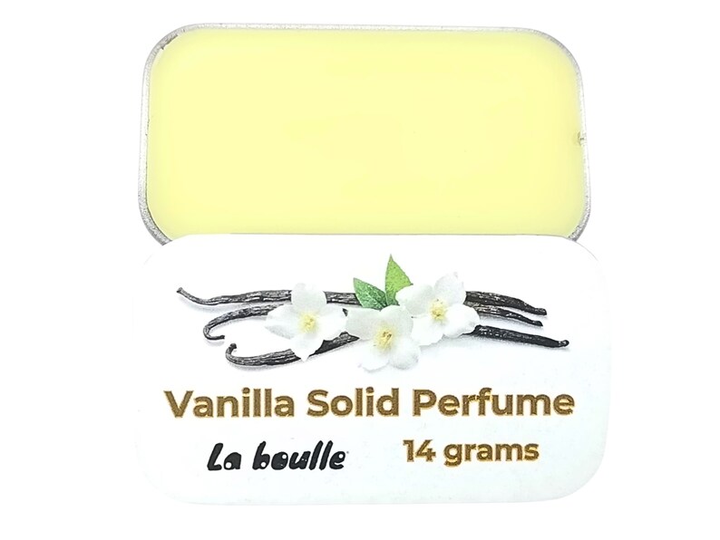 May include: A white tin with a yellow solid perfume inside. The tin has a label that says "Vanilla Solid Perfume" and "La Bouille" with a vanilla bean and white flower design.