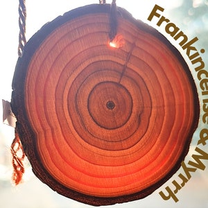 May include: A wooden slice with concentric rings, hanging from a rope. The text "Frankincense & Myrrh" is written in gold lettering on a blurred background.