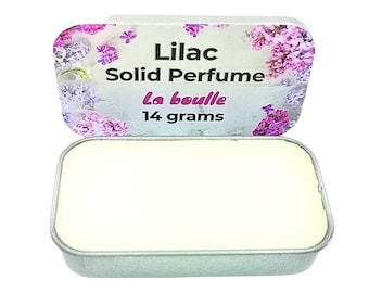 May include: A small, round tin with a floral design and the text "Lilac Solid Perfume la bouille 14 grams". The tin is open and shows a white solid perfume inside.
