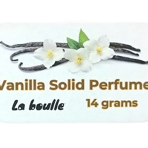 May include: A white tin with a gold label that reads "Vanilla Solid Perfume La Bouille 14 grams". The label also features a design of vanilla beans and white flowers.
