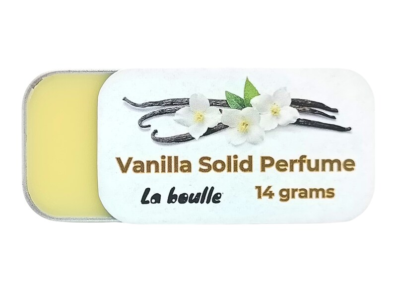 May include: A small, round tin container with a white label that reads "Vanilla Solid Perfume La bouille 14 grams". The label features a graphic of vanilla beans and white flowers.