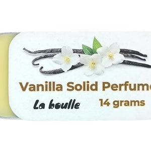 May include: A small, white tin with a gold lid contains a solid vanilla perfume. The tin has a label with the text "Vanilla Solid Perfume", "La Bouille", and "14 grams". The label also features a graphic of vanilla beans and white flowers.