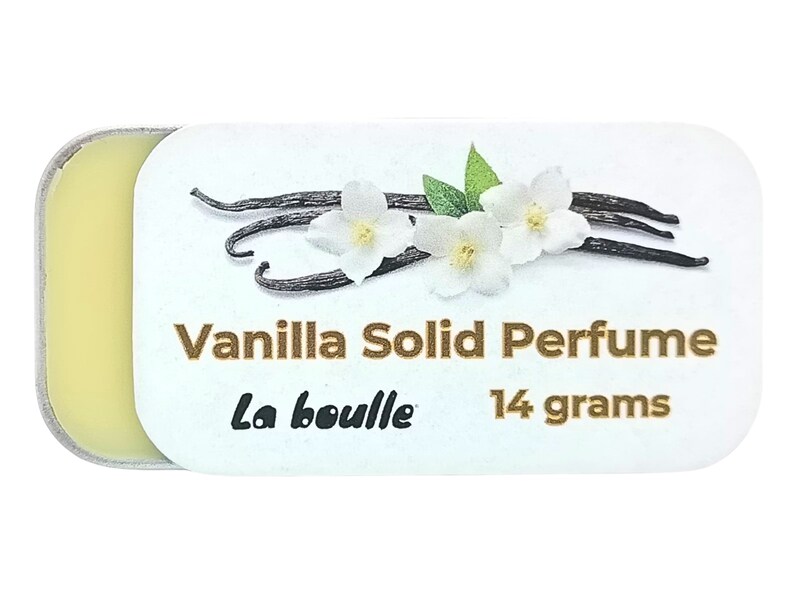 May include: A small, white tin with a gold lid contains a solid vanilla perfume. The tin has a label with the text "Vanilla Solid Perfume", "La Bouille", and "14 grams". The label also features a graphic of vanilla beans and white flowers.