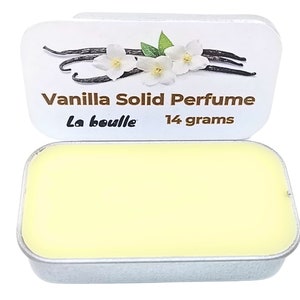 Op de afbeelding: Een klein, zilveren blikje met een wit etiket waarop "Vanilla Solid Perfume La Bouille 14 gram" staat. Het etiket bevat ook een tekening van vanillebonen en witte bloemen. Het blikje is open en laat een gele vaste parfum zien.
