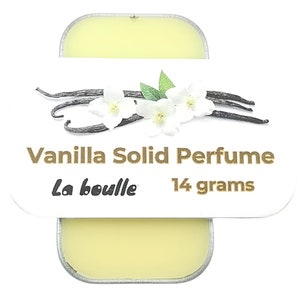 May include: A small, white tin with a gold label that reads "Vanilla Solid Perfume La bouille 14 grams". The label also features a graphic of vanilla beans and white flowers.