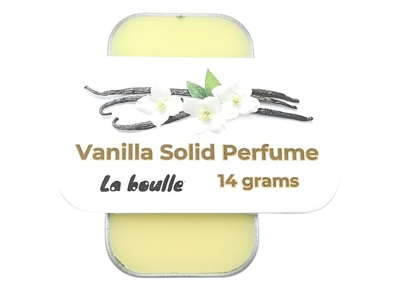 May include: A small, white tin with a gold label that reads "Vanilla Solid Perfume La bouille 14 grams". The label also features a graphic of vanilla beans and white flowers.