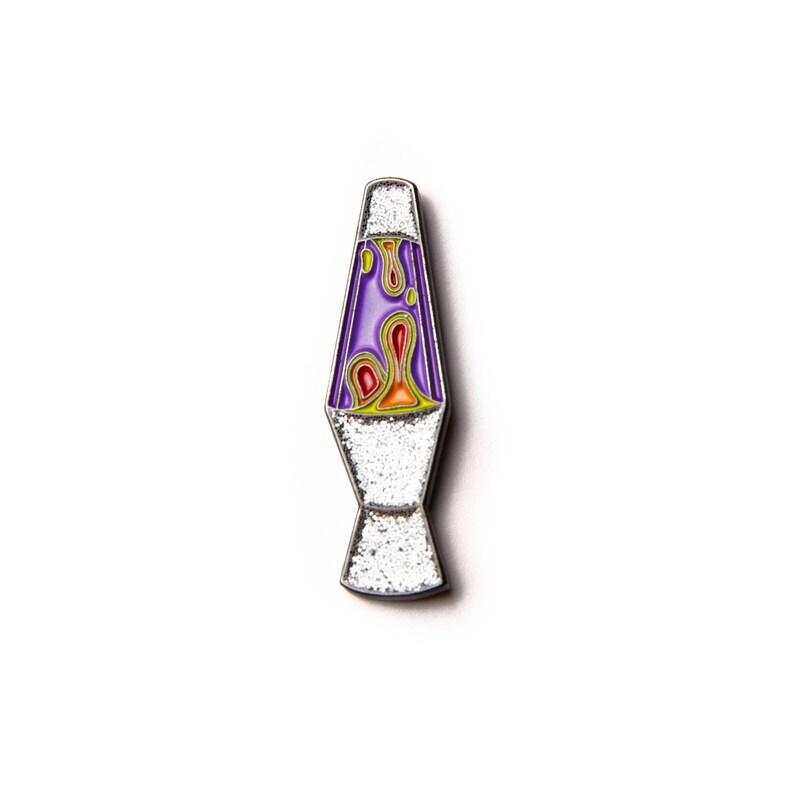 May include: A silver metal pin shaped like a lava lamp with a purple base and orange and yellow lava inside.
