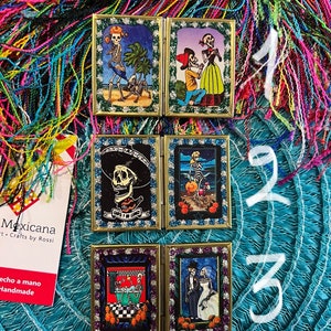May include: Four small, framed, hinged, decorative boxes with colorful images of skeletons in various scenes. The boxes are decorated with glitter and have gold frames. The boxes are arranged in two rows of two. The boxes are on a blue and green background.