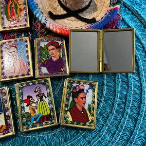 May include: A collection of small, framed, decorative images with gold trim. The images feature various subjects, including religious figures, a woman with flowers in her hair, and a couple dressed as skeletons. The images are arranged on a blue and white patterned surface.