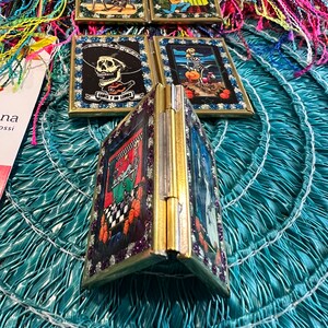 May include: A set of five small, framed, decorative mirrors with gold frames. Each mirror features a different Day of the Dead themed image. The mirrors are arranged in a circle on a blue and green surface.