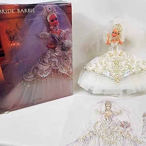 Peut inclure: Une poupée Barbie Empress Bride dans une robe de mariée blanche avec des broderies dorées et un voile. La poupée est exposée à côté de sa boîte et d'une esquisse de la poupée. La boîte porte les mots "Empress Bride Barbie".