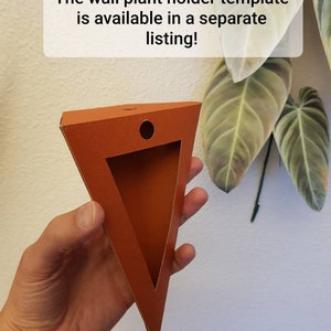 Pu&ograve; includere: Un modello di supporto a parete triangolare arancione per piante, con un ritaglio e un foro circolare. Il testo sull'immagine recita: "Il modello di supporto a parete &egrave; disponibile in un annuncio separato!"