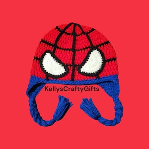 May include: Red and black crocheted hat with a white spider design and blue ear flaps. The hat has a black crocheted brim and blue tassels on the ear flaps. The text "KellysCraftyGifts" is visible on the hat.