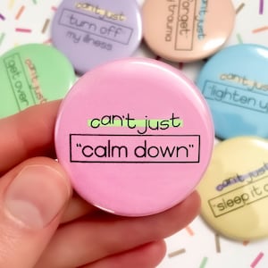 K&ouml;nnte beinhalten: Ein Set aus sechs rosa, gr&uuml;nen, blauen, gelben und violetten Anstecknadeln mit dem Text "can't just" und einem anderen Spruch auf jeder Nadel. Der Spruch auf der rosa Nadel lautet "calm down".