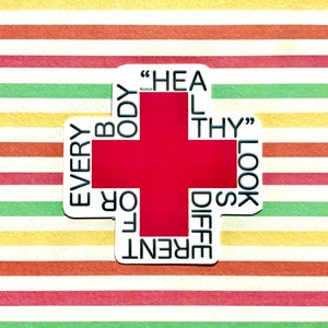 May include: A white sticker with a red cross in the center. The words "EVERY BODY LOOKS DIFFERENT" are written around the cross. The text "HEAL THY" is written inside the cross.