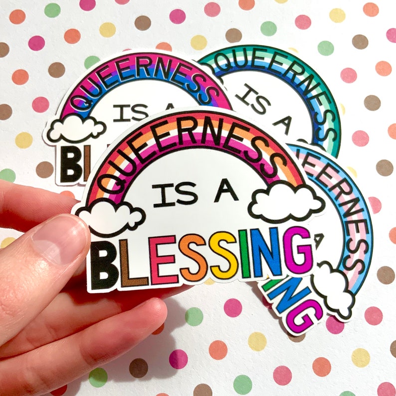 May include: Four rainbow-colored stickers with the text "Queerness is a Blessing" in black lettering. The stickers are arranged in a stack, with the top sticker showing the full text and the other stickers showing only parts of the text.