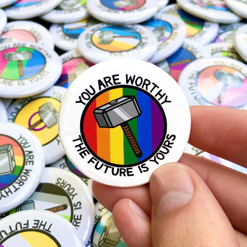 Puede incluir: Un bot&oacute;n blanco con un c&iacute;rculo arco&iacute;ris y un martillo plateado con un mango marr&oacute;n. El texto "You are worthy the future is yours" est&aacute; escrito alrededor del c&iacute;rculo.