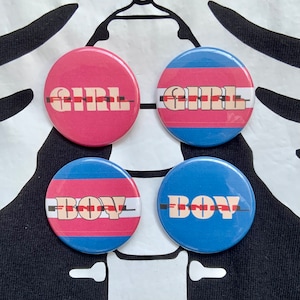 Peut inclure: Quatre boutons ronds avec des rayures bleues et roses. Les boutons portent les mots "GIRL" et "BOY" écrits dans une police de caractères stylisée.