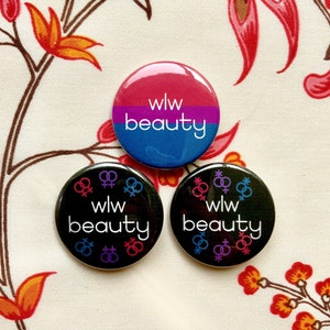 May include: Three circular badges with the words "wlw beauty". One has a pink, purple, and blue gradient. The other two are black with colourful symbols and text. The badges are displayed on a floral patterned background.