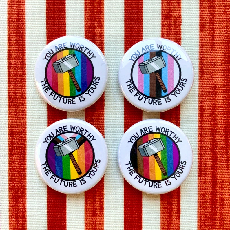 Puede incluir: Cuatro botones redondos blancos con el texto "You are worthy, the future is yours" y un martillo plateado con un mango de madera sobre un fondo arco&iacute;ris. Los colores del arco&iacute;ris son rojo, naranja, amarillo, verde, azul, &iacute;ndigo y violeta.