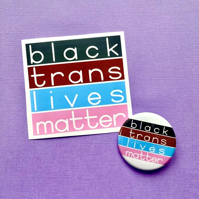 Puede incluir: Una pegatina blanca con el texto "black trans lives matter" en letras negras y rosas sobre un fondo morado. Un bot&oacute;n redondo con el mismo texto en letras negras y rosas sobre un fondo blanco.