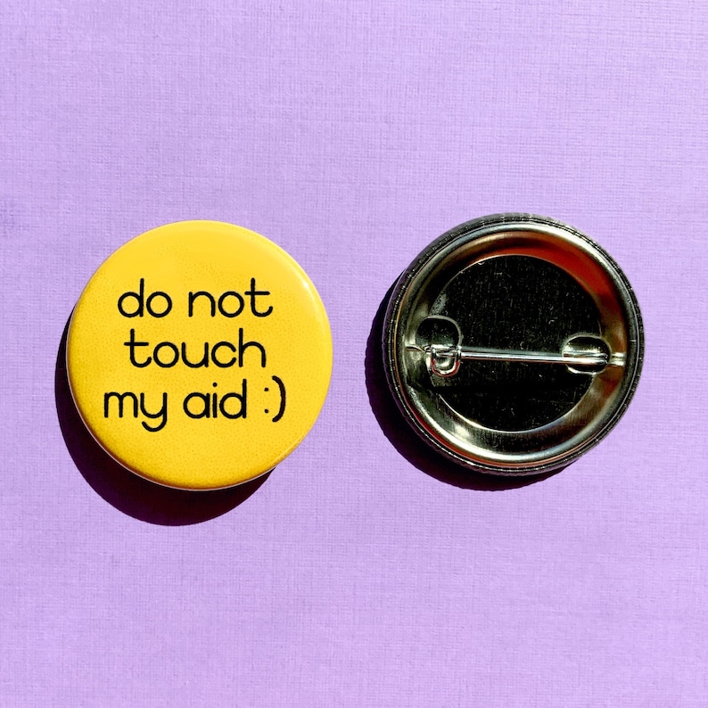 May include: Yellow button with black text that reads "do not touch my aid :)". The button is on a purple background.