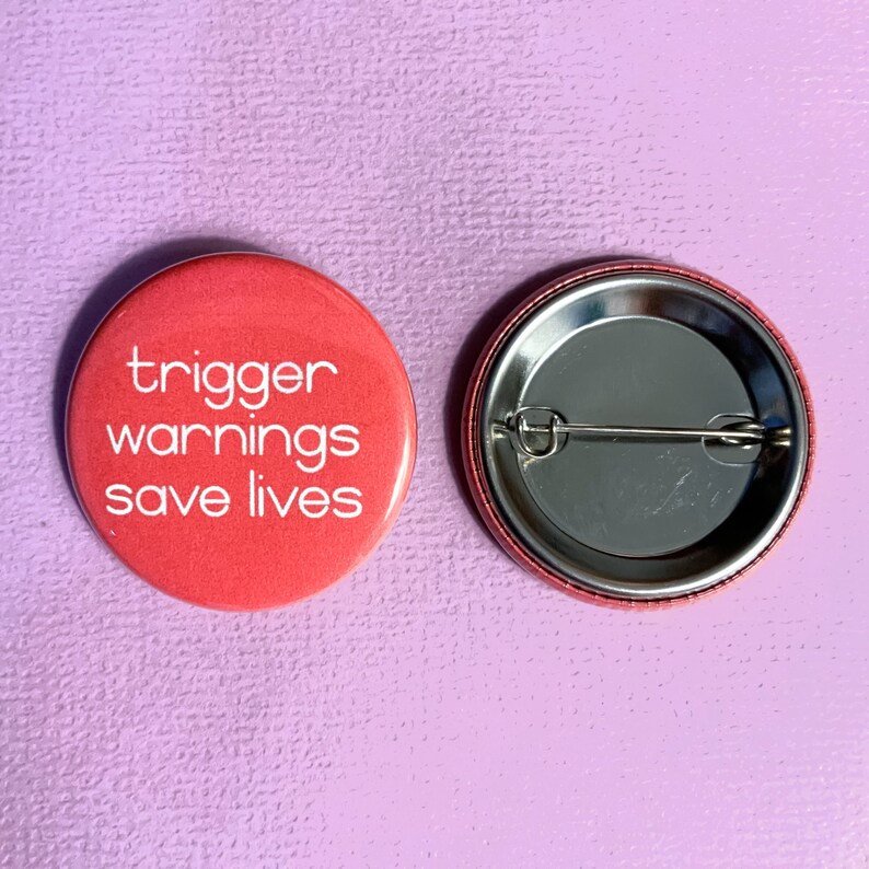 May include: A red button with the text "trigger warnings save lives" in white lettering. The back of the button is silver with a safety pin.