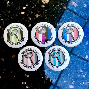 Puede incluir: Cinco botones redondos con el texto "You are worthy, the future is yours" y una imagen de dibujos animados de un martillo plateado. Cada bot&oacute;n tiene un patr&oacute;n de rayas de color diferente: verde, morado, azul, rosa y azul claro.