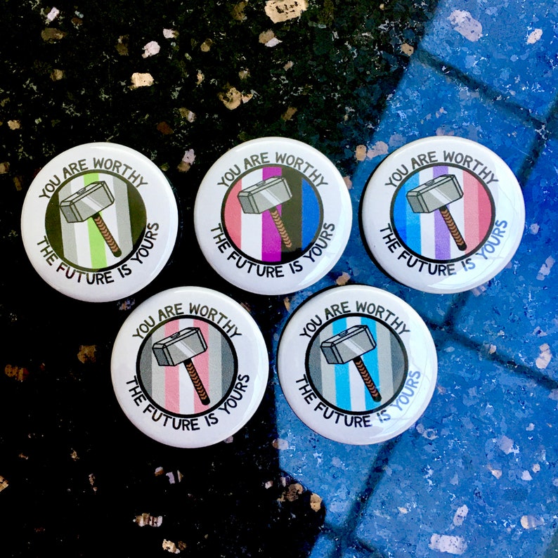 Puede incluir: Cinco botones redondos con el texto "You are worthy, the future is yours" y una imagen de dibujos animados de un martillo plateado. Cada bot&oacute;n tiene un patr&oacute;n de rayas de color diferente: verde, morado, azul, rosa y azul claro.