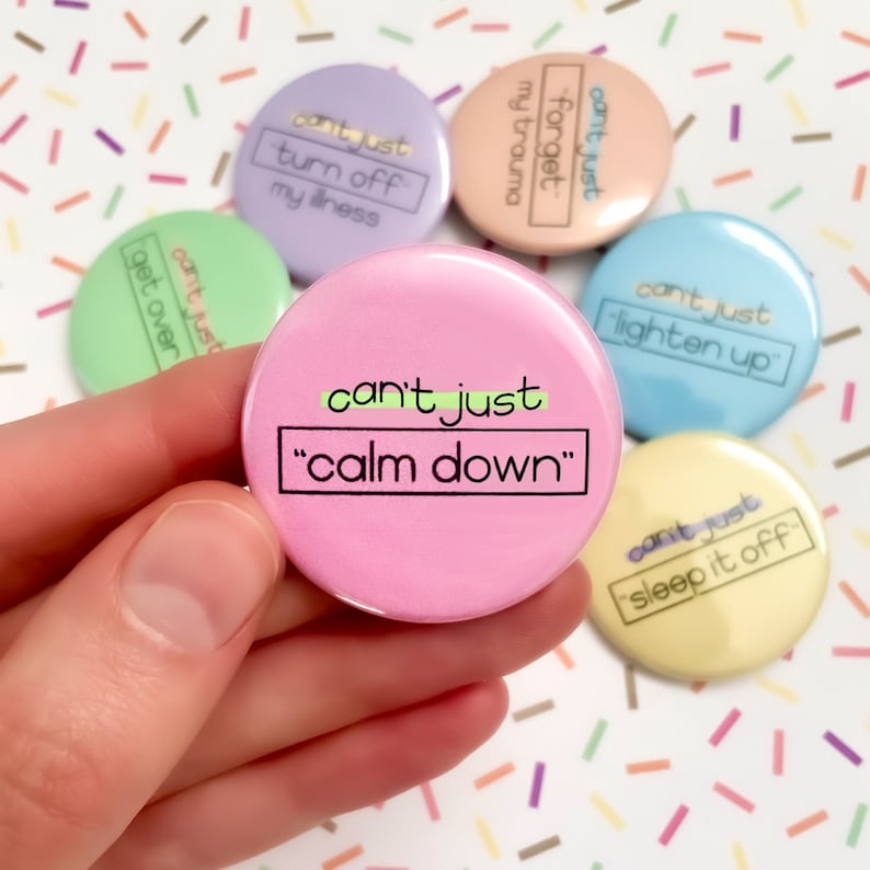 K&ouml;nnte beinhalten: Ein Set aus sechs rosa, gr&uuml;nen, blauen, gelben und violetten Anstecknadeln mit dem Text "can't just" und einem anderen Spruch auf jeder Nadel. Der Spruch auf der rosa Nadel lautet "calm down".