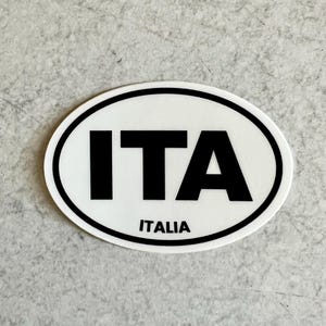 May include: White oval sticker with black text that reads "ITA" and "ITALIA".