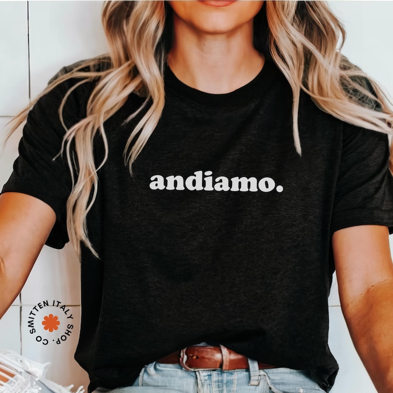 May include: A black t-shirt with the text "andiamo." printed in white on the front. The shirt is being worn by a person with long blonde hair.
