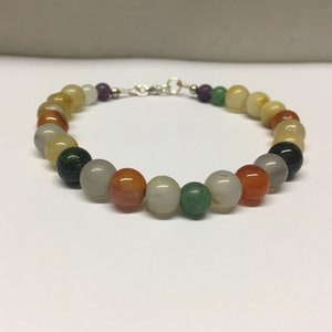 Peut inclure: Un bracelet en perles multicolores avec un fermoir argenté. Les perles sont de différentes nuances de vert, marron, orange et blanc.