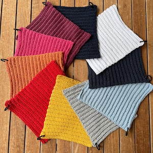 Könnte beinhalten: Zehn gehäkelte Topflappen in verschiedenen Farben, darunter Rot, Orange, Gelb, Grün, Blau und Weiß. Die Topflappen sind in einem Kreis auf einer Holzoberfläche angeordnet.