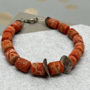 Può includere: Un braccialetto realizzato con perline a motivi arancioni e bianchi e dettagli argentati.