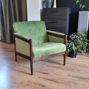 May include: A green velvet armchair with dark wood frame legs. The chair is sitting on a wood floor.