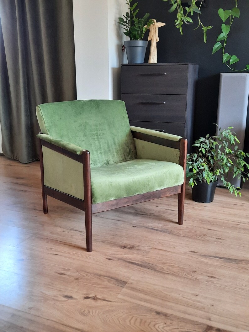 May include: A green velvet armchair with dark wood frame legs. The chair is sitting on a wood floor.