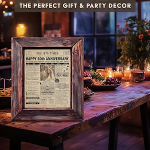 May include: A framed vintage newspaper print with the headline "The 1975 Times" and the text "Happy 50th Anniversary" with a photo of a couple. The print is on a wooden table with a bowl of fruit and candles in the background.