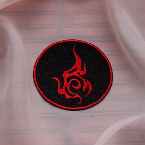 May include: A red and black embroidered patch with a stylised flame design. The patch is circular and has a black background with a red flame design.