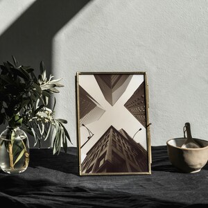 May include: A gold-toned picture frame with a black and white photograph of a city skyline. The frame is sitting on a black surface with a vase of greenery and a small bowl.