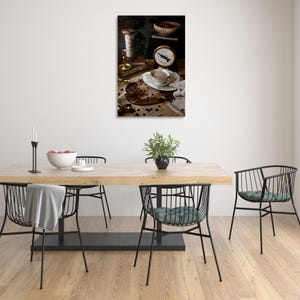 K&ouml;nnte beinhalten: Ein Stilllebenfoto einer Tasse Kaffee, Kaffeebohnen, einer Waage und einer Garnrolle auf einem Holztisch. Die Kaffeetasse ist wei&szlig; mit goldfarbenem Rand und mit Kaffee gef&uuml;llt. Die Kaffeebohnen sind um die Tasse und die Waage herum verstreut. Die Waage ist alt und hat ein Messingzifferblatt. Die Garnrolle ist braun und mit einem wei&szlig;en Band gebunden.