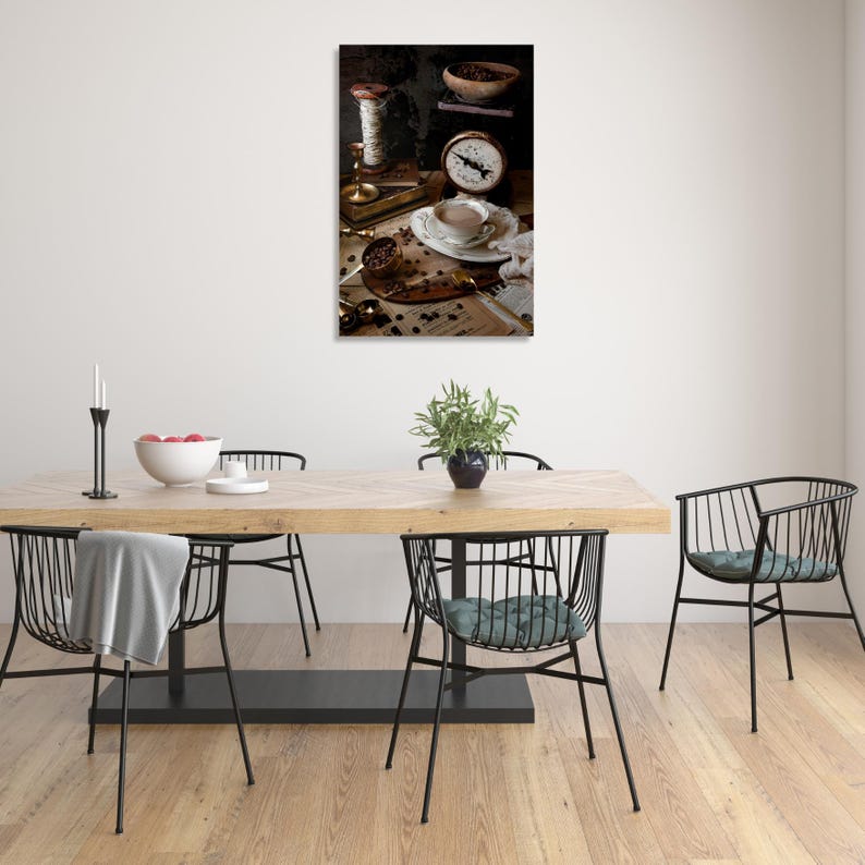 K&ouml;nnte beinhalten: Ein Stilllebenfoto einer Tasse Kaffee, Kaffeebohnen, einer Waage und einer Garnrolle auf einem Holztisch. Die Kaffeetasse ist wei&szlig; mit goldfarbenem Rand und mit Kaffee gef&uuml;llt. Die Kaffeebohnen sind um die Tasse und die Waage herum verstreut. Die Waage ist alt und hat ein Messingzifferblatt. Die Garnrolle ist braun und mit einem wei&szlig;en Band gebunden.