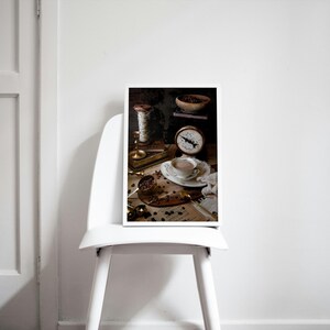 K&ouml;nnte beinhalten: Ein Stillleben-Foto einer Tasse Kaffee, einer antiken Waage und Kaffeebohnen auf einem Tisch. Die Kaffeetasse ist wei&szlig; mit goldfarbenem Rand und mit einer hellbraunen Fl&uuml;ssigkeit gef&uuml;llt. Die Waage ist aus Messing und hat ein wei&szlig;es Zifferblatt mit schwarzen Zahlen. Die Kaffeebohnen sind auf dem Tisch verstreut.