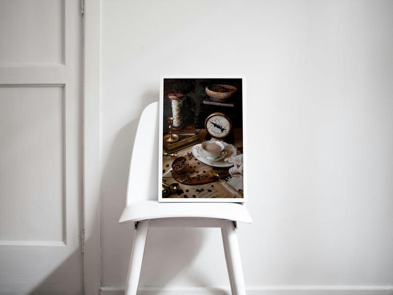 K&ouml;nnte beinhalten: Ein Stillleben-Foto einer Tasse Kaffee, einer antiken Waage und Kaffeebohnen auf einem Tisch. Die Kaffeetasse ist wei&szlig; mit goldfarbenem Rand und mit einer hellbraunen Fl&uuml;ssigkeit gef&uuml;llt. Die Waage ist aus Messing und hat ein wei&szlig;es Zifferblatt mit schwarzen Zahlen. Die Kaffeebohnen sind auf dem Tisch verstreut.