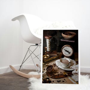 K&ouml;nnte beinhalten: Eine Vintage-Stillleben mit einer Tasse Kaffee, einer Waage, einer Garnrolle und Kaffeebohnen auf einem St&uuml;ck Papier mit Noten.