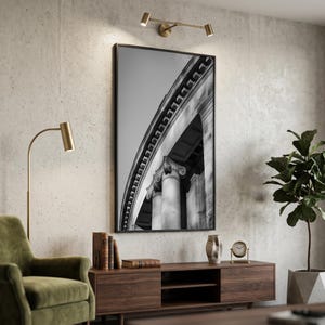 Puede incluir: Impresión en blanco y negro enmarcada de detalles arquitectónicos, con columnas y adornos. La impresión se exhibe en un salón moderno con un sillón verde, un mueble de madera y una planta en maceta. Iluminación con una lámpara de latón.