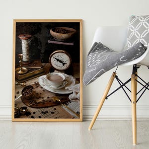 K&ouml;nnte beinhalten: Eine Stilllebenfotografie einer Tasse Kaffee, einer Waage, einer Garnrolle und Kaffeebohnen auf einem Tisch. Das Foto ist in einem braunen Rahmen.