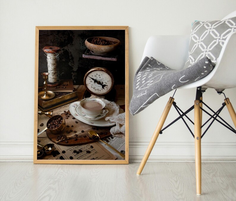 K&ouml;nnte beinhalten: Eine Stilllebenfotografie einer Tasse Kaffee, einer Waage, einer Garnrolle und Kaffeebohnen auf einem Tisch. Das Foto ist in einem braunen Rahmen.