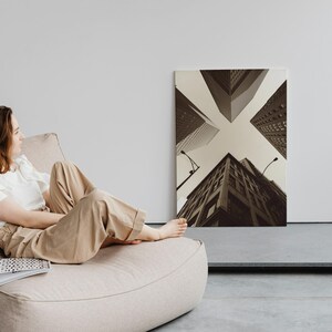May include: A woman relaxes in a beige beanbag chair, looking towards a black and white photograph of city buildings. The photograph is hanging on a white wall.